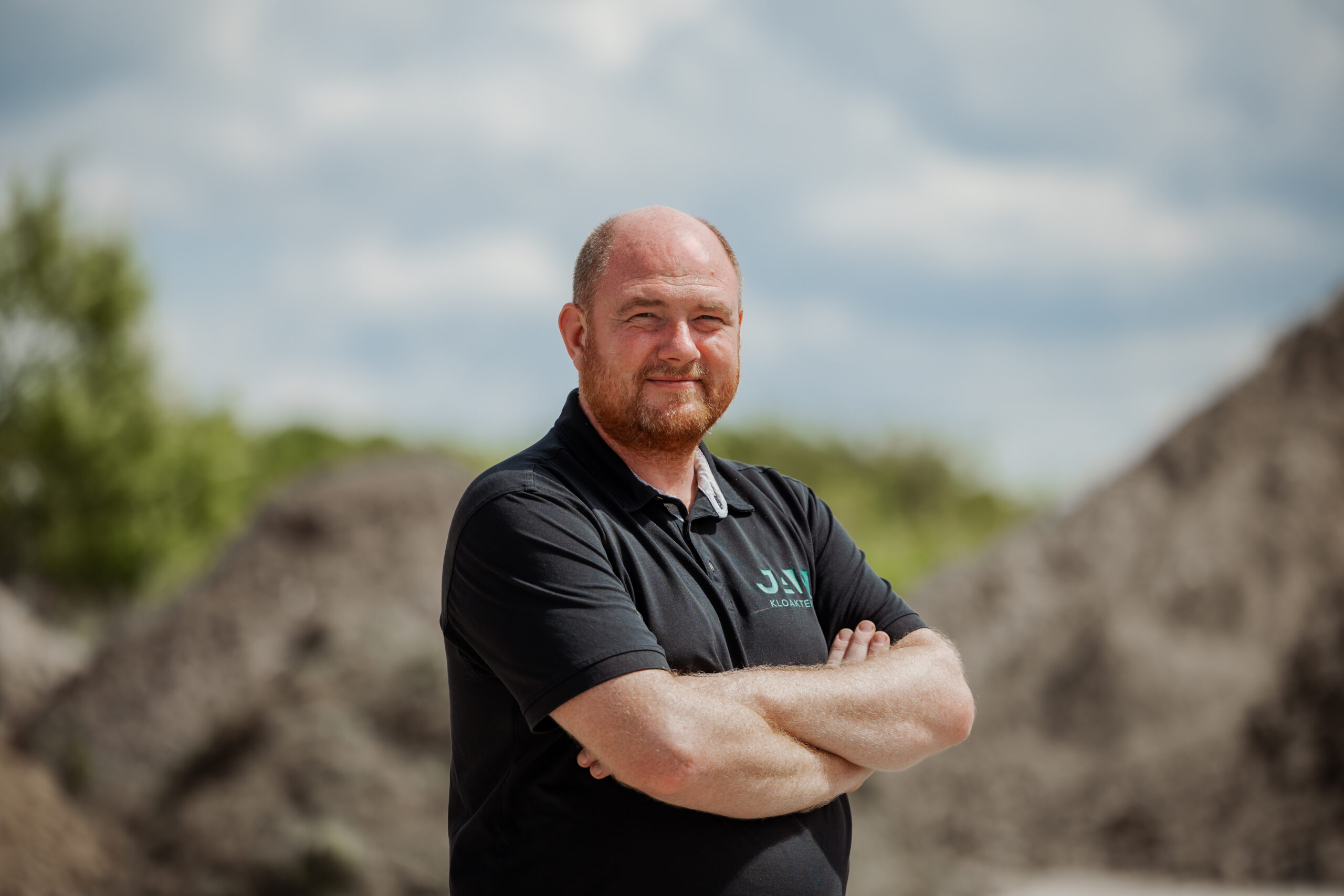 Paw fra JAC Kloakteknik står med armene over kors foran byggeplads.