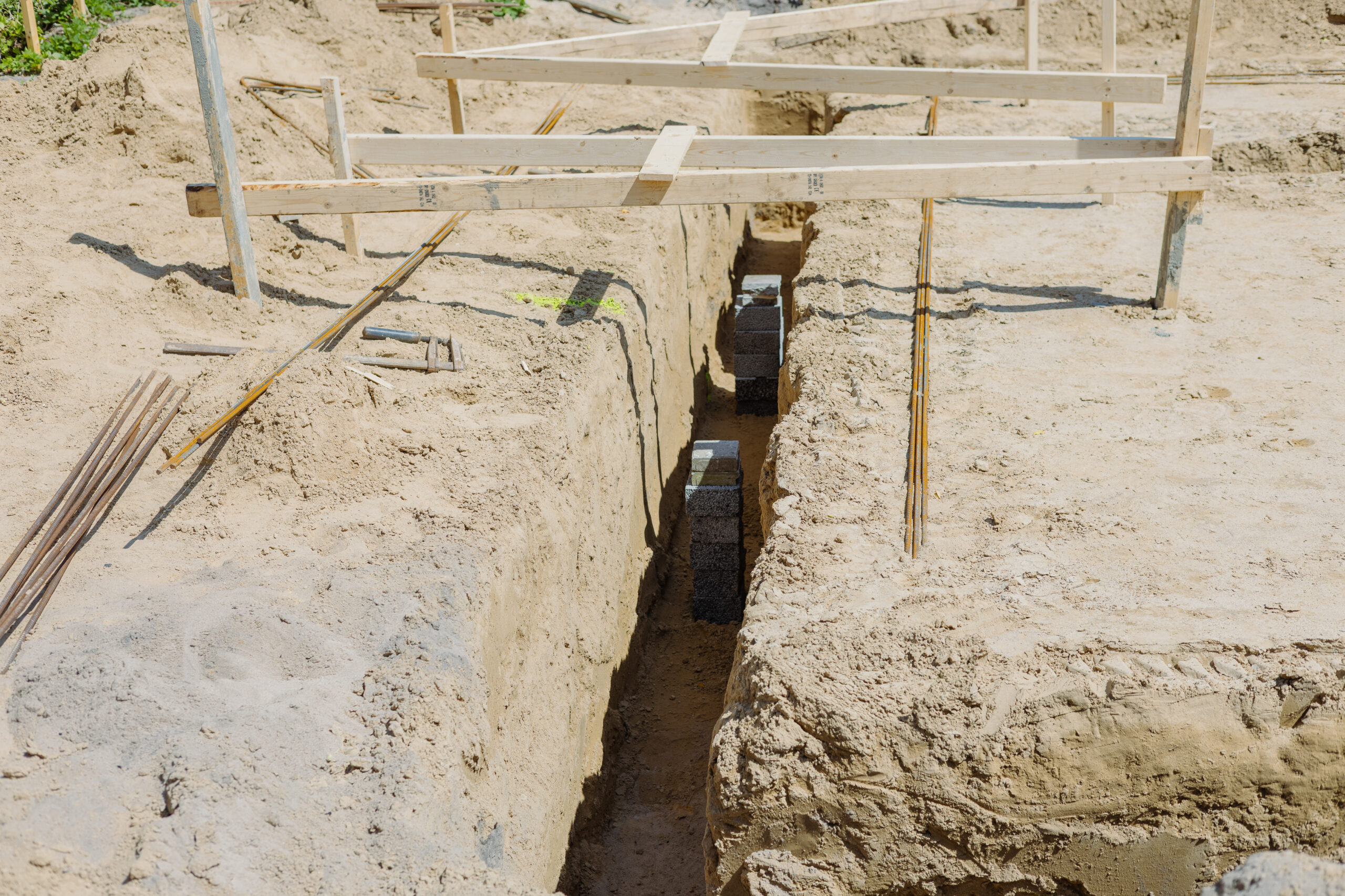 Udgravning omkring bygning med synlige støtteklodser og armeringsjern.