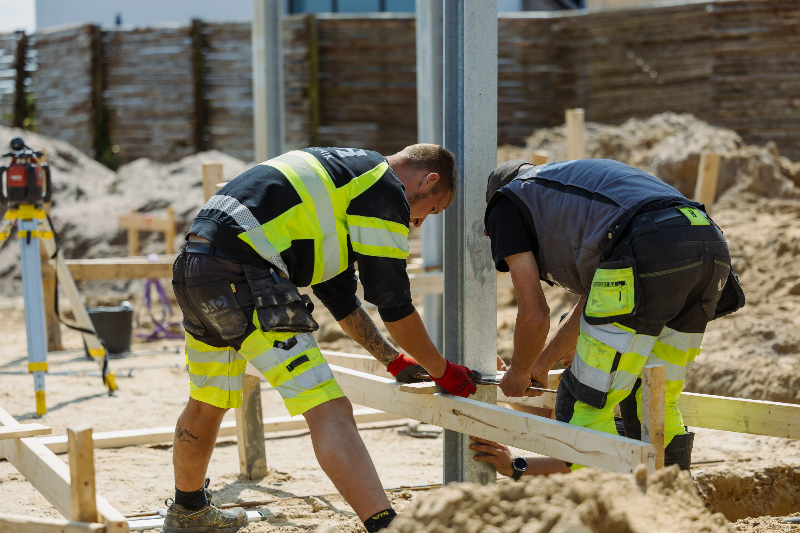 To personer arbejder med udmåling og trærammer på byggeplads.