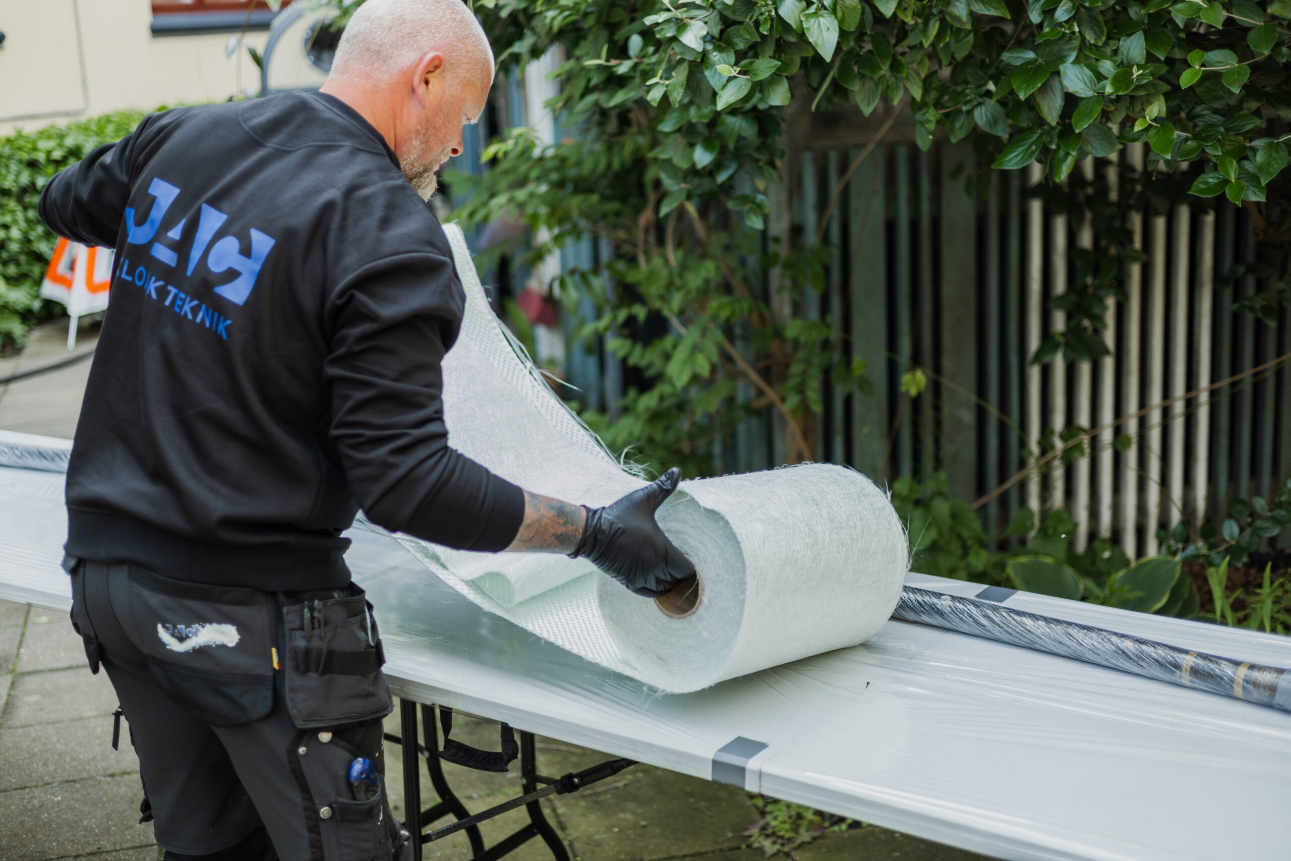 Mand ruller glasfiberdug ud til strømpeforing på arbejdsbord.